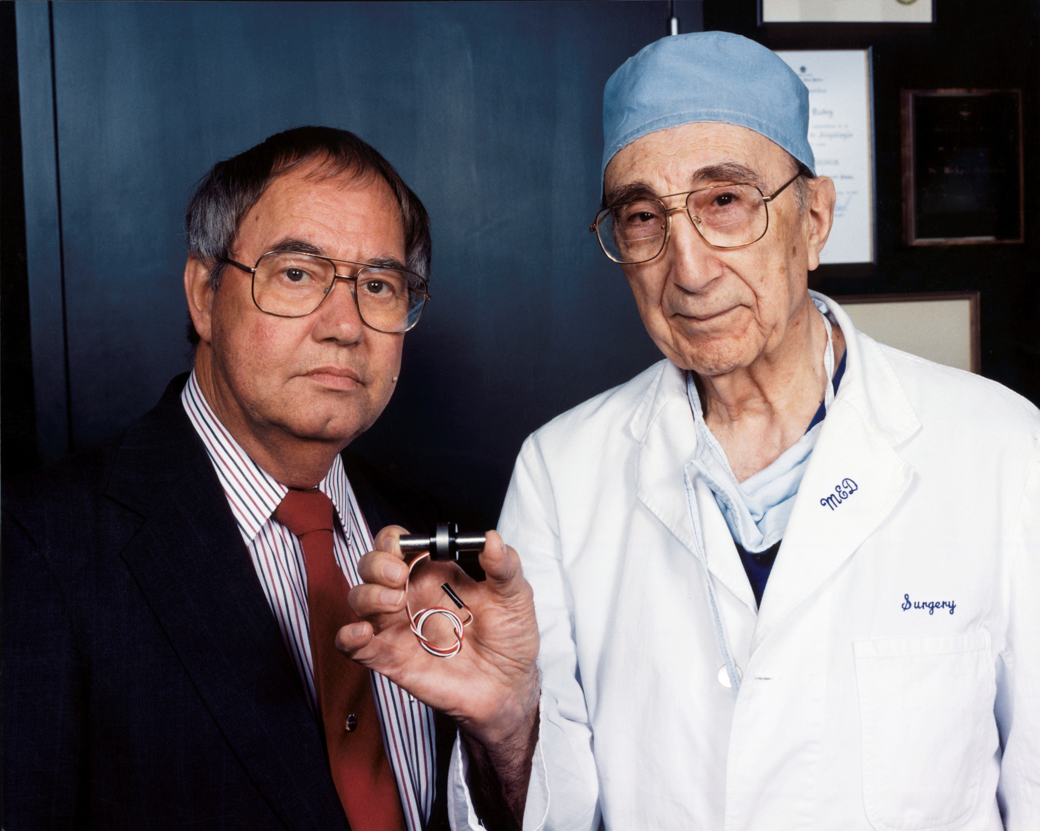 Доктор Майкл Дебейки (справа) держит MicroMed-DeBakey VAD (устройство для помощи желудочкам), крошечный насос для помощи сердцу. С ним один из его пациентов, перенесших операцию по пересадке сердца, Дэвид Саусье, инженер Космического центра имени Джонсона
