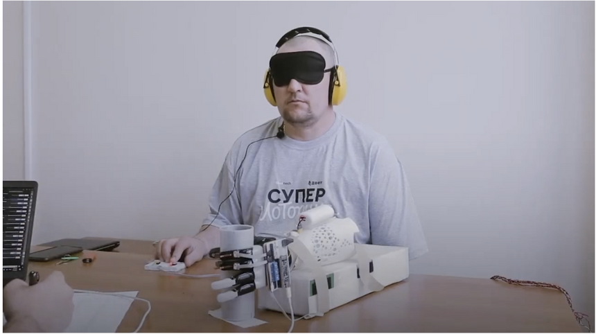 Пациент с повязкой на глазах определяет размер предмета (серая труба) по обратной связи от протеза руки, который с этим предметом контактирует